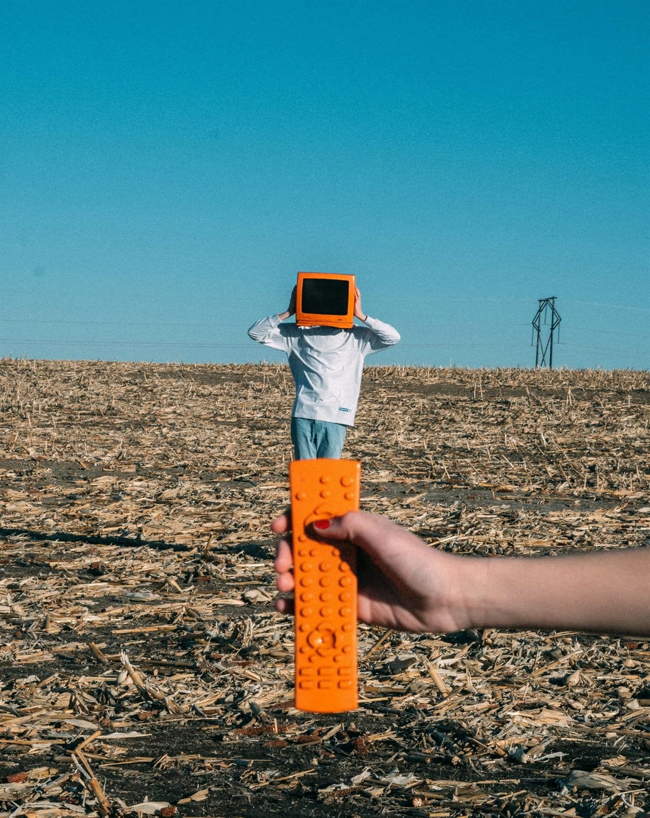 A person in a field holding an oversized remote, with a retro screen for a head